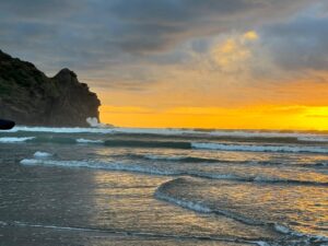 Waves breaking on a shoreline beneath a headland at sunset