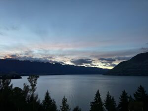 A still lake at dusk beneath a soft pink and blue evening sky, hills darkening on the far shore