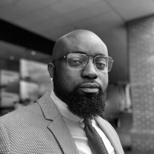 Kingsley A. Boateng, Integrative Psychotherapeutic Counsellor, Clinical Supervisor and Civil and Commercial Mediator, in a black and white head and shoulders portrait wearing glasses, a jacket and a tie